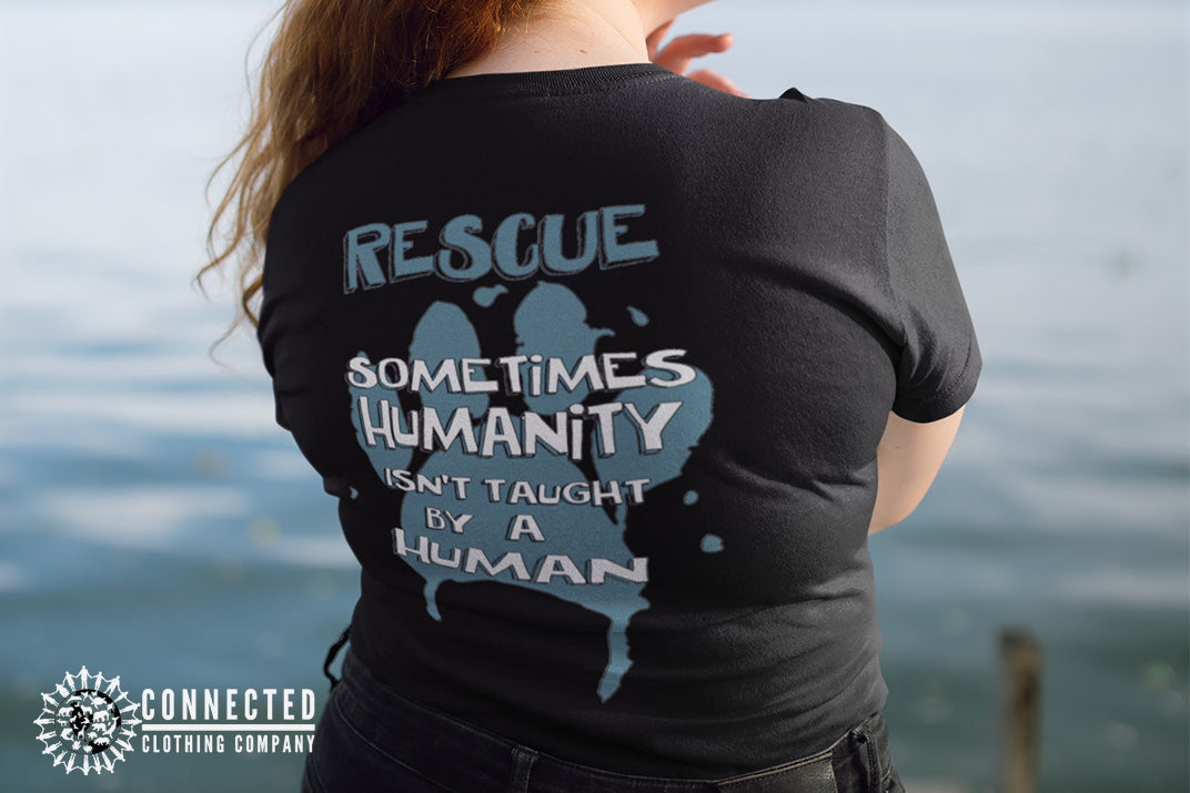 Model wearing Black Show Humanity Tee at the lake that reads "Rescue. Sometimes humanity isn't taught by a human" - architectconstructor - Ethically and Sustainably Made - 10% donated to the Society for the Prevention of Cruelty to Animals
